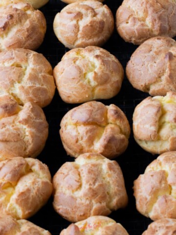 over a dozen golden brown choux pastry puffs closely spaced together on a cooling rack.